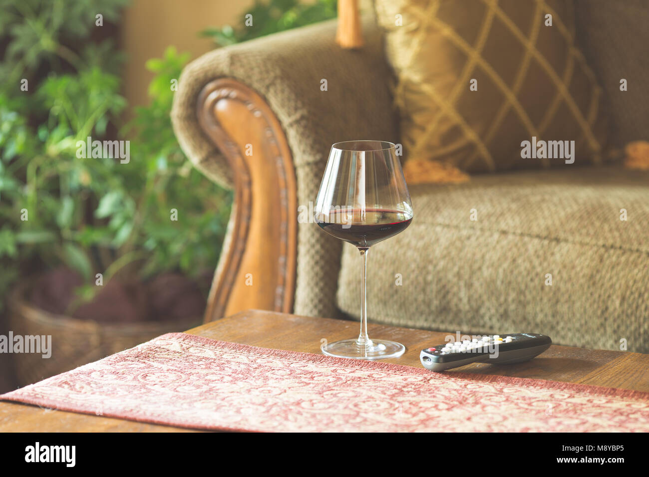 A glass of red wine on a coffee table next to the TV remote Stock Photo