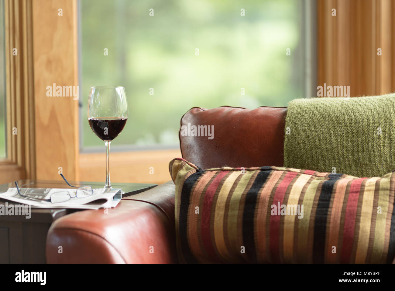 A glass of red wine on a table next to a newspaper and reading glasses Stock Photo