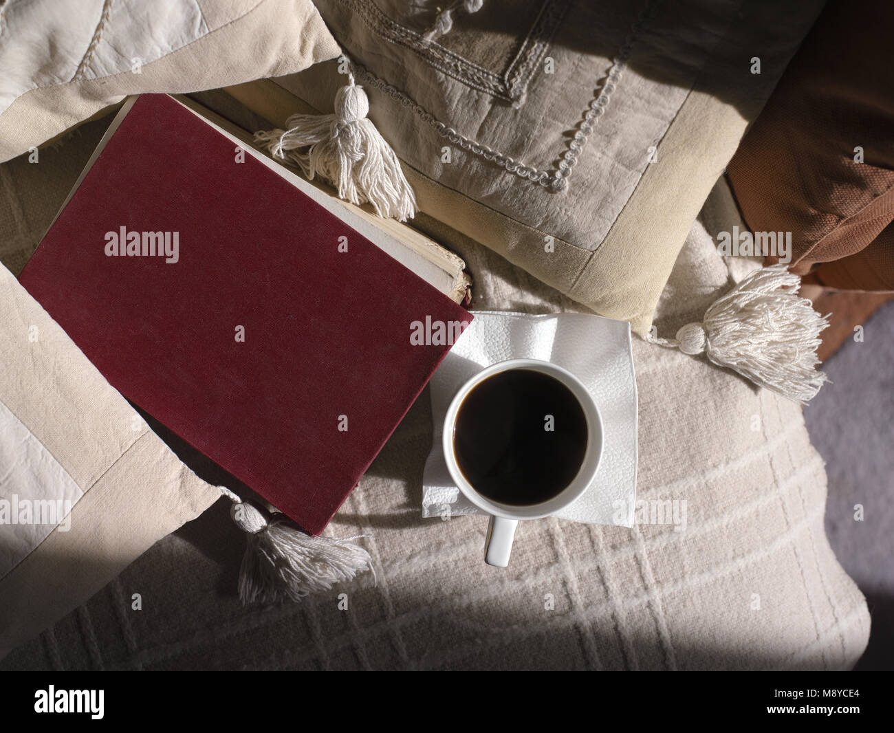 Red book and cup of coffee on a sofe covered with blanket and pillows, above view Stock Photo
