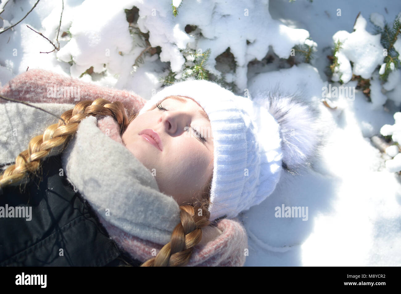 A young woman with warm clothes and closed eyes is lying in snow. A daydream scene. Stock Photo
