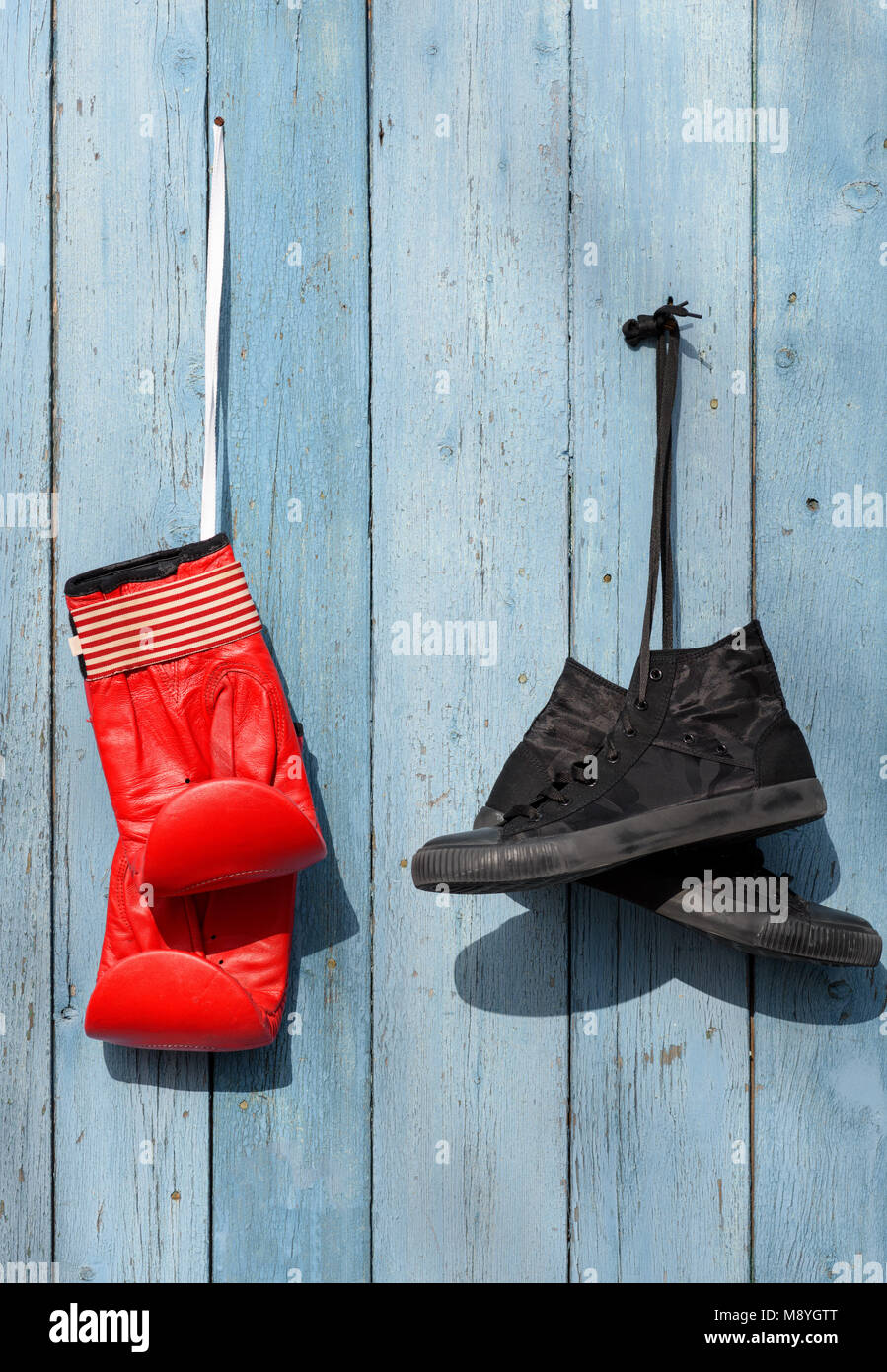 Black textile worn sneakers and red leather boxing gloves hanging on a blue wooden wall Stock Photo