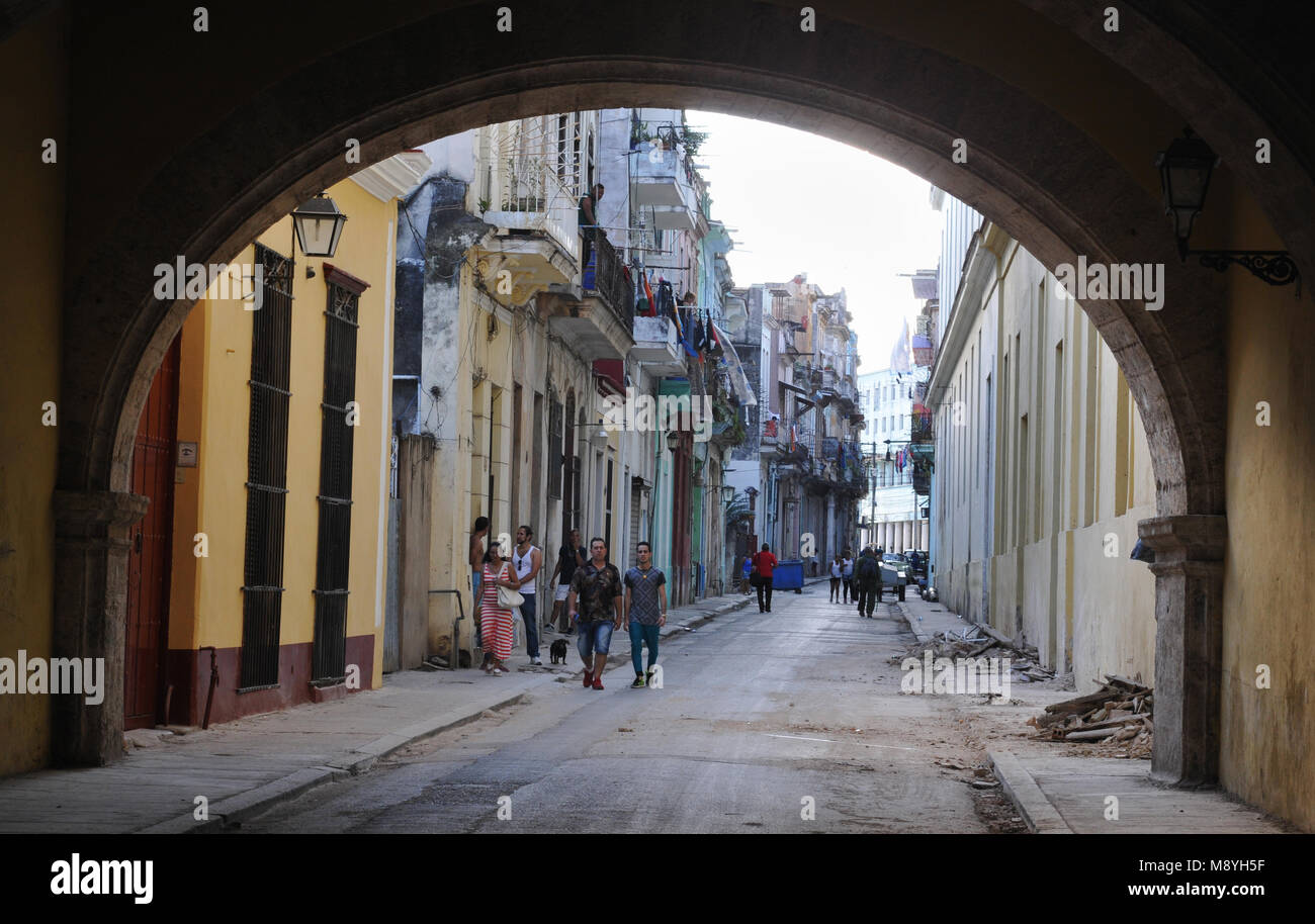 People walk along a street lined with colourful buildings towards an archway in Old Havana, Cuba. Stock Photo