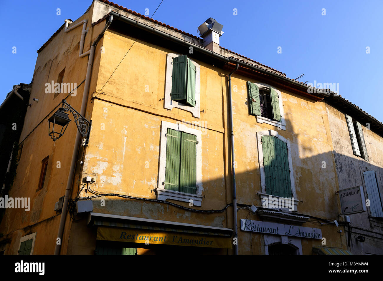 Street scene in Arles, yellow traditional house with green shutters and vintage restaurant sign, Provence, France Stock Photo