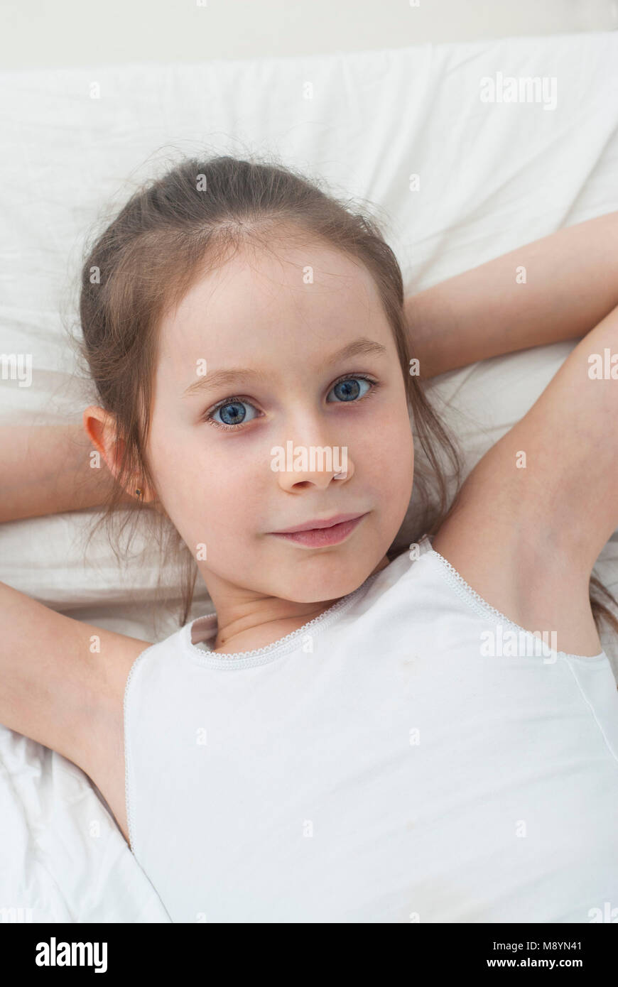 Portret of Adorable Little Girl with Blue Eyes,Awaked up in her bed. Morning. flat Lay. Stock Photo