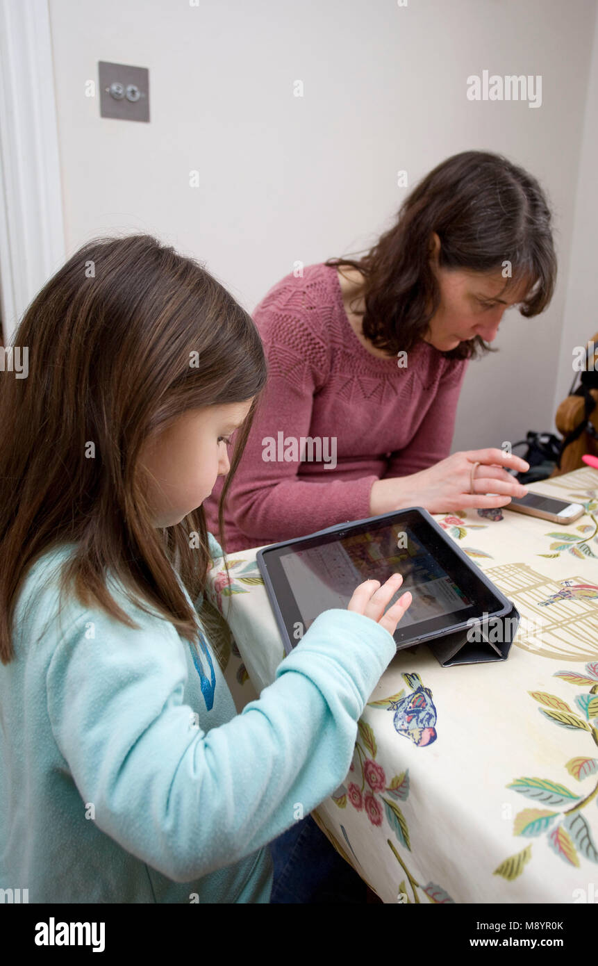 mother and daughter on iPhone and iPad at the kitchen table Stock Photo