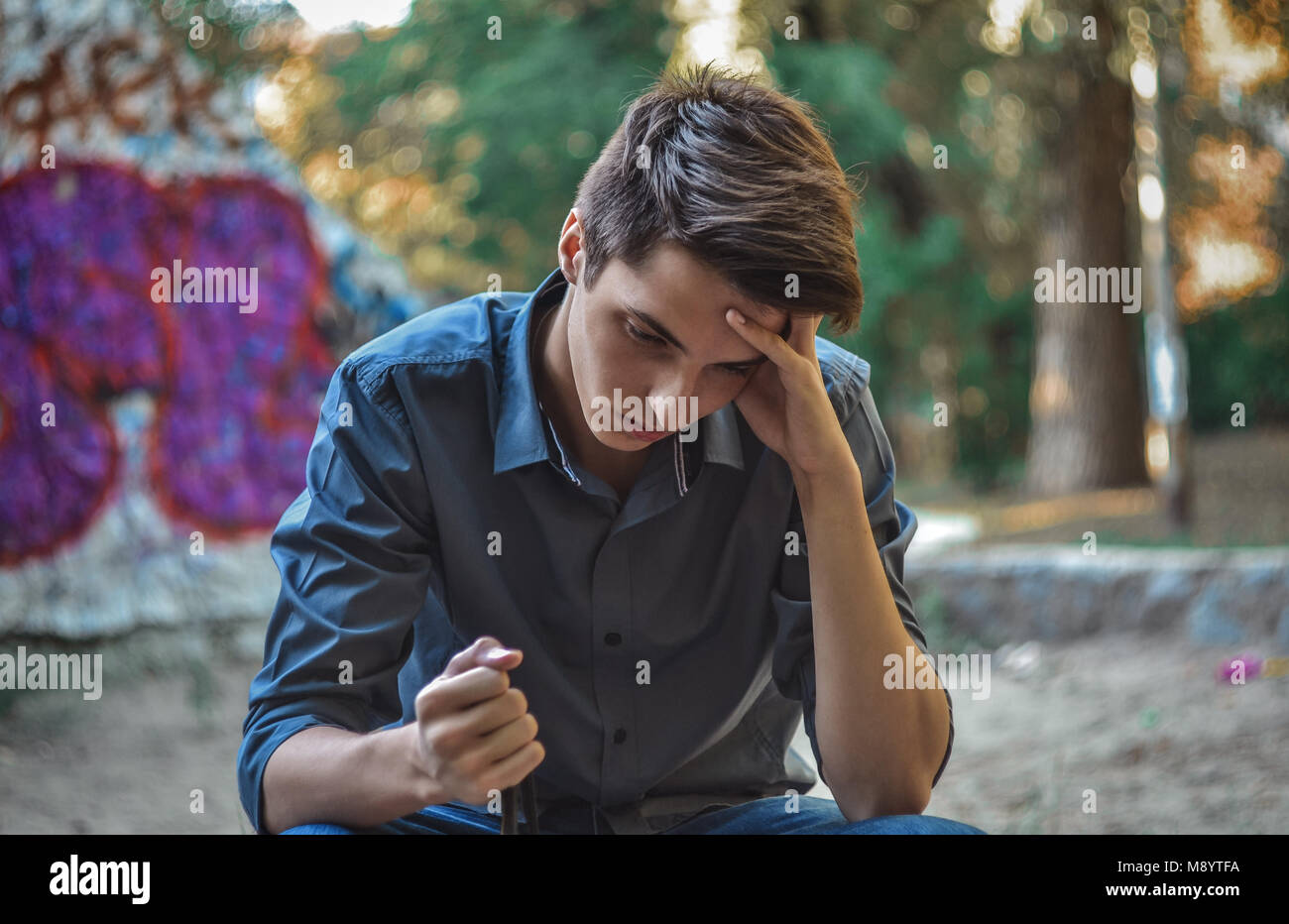 Worried teenage boy sitting holding head thinking how to solve problems Stock Photo