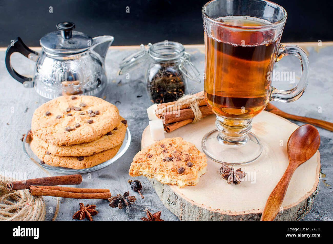 stack of homemade cookies with chocolate drops, сup of hot black tea, cinnamon, anise on dark