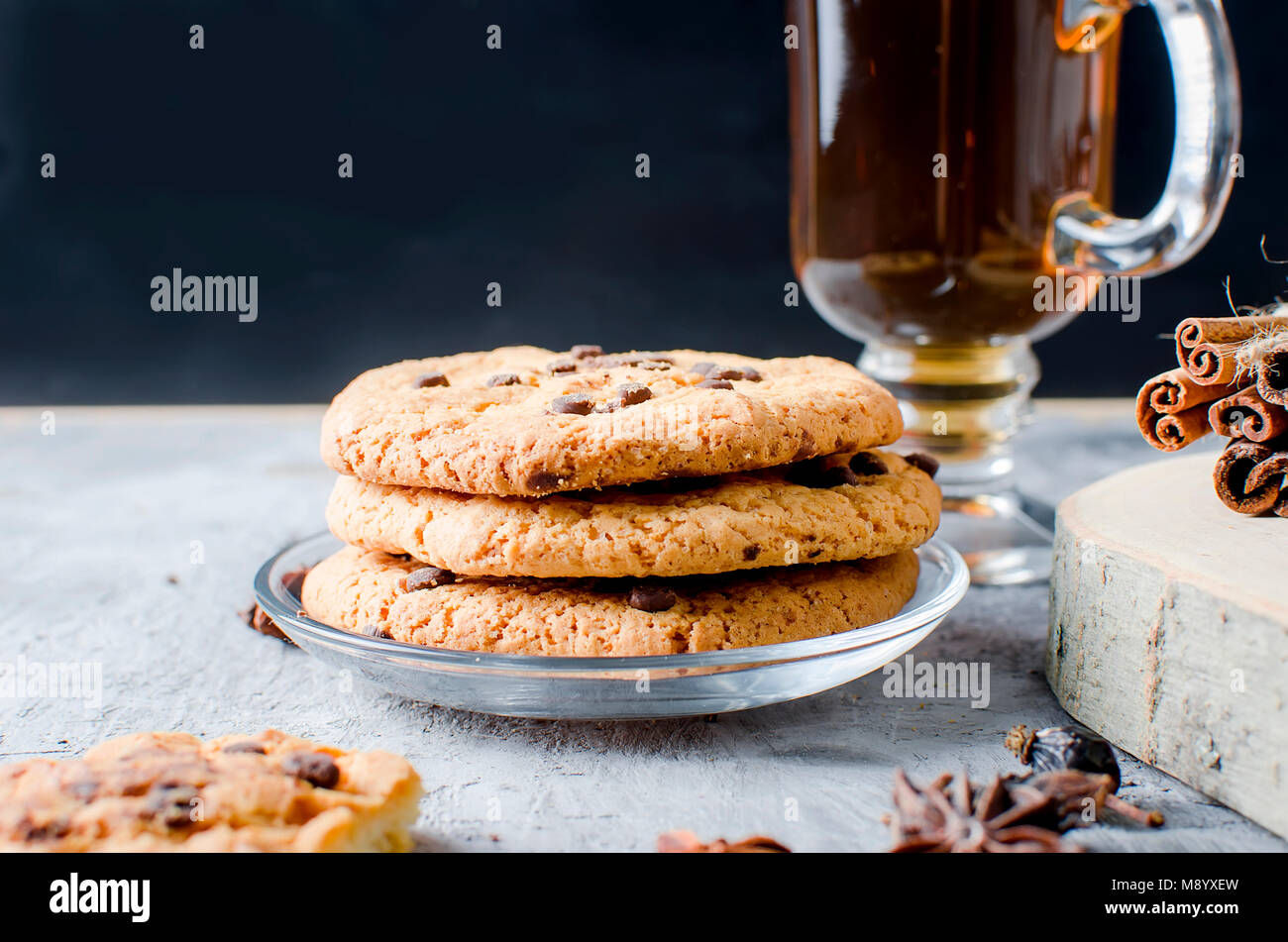 stack of homemade cookies with chocolate drops, сup of hot black tea, cinnamon, anise on dark