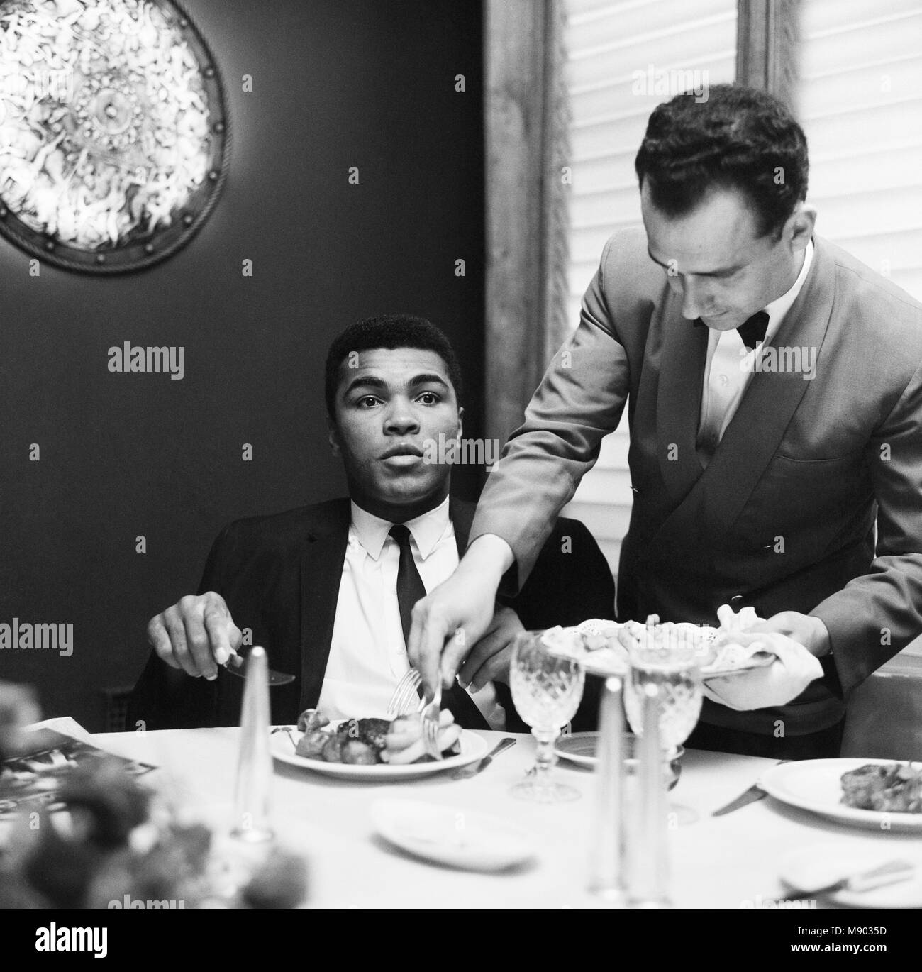 Cassius Clay (Pictured) having lunch in London before his trip to Scotland for an exhibition bout against fellow American Jimmy Ellis. However, his visit didn't go to plan after fans booed during the exhibition fight. The World Champion berated them saying: 'All booing must stop when the king's in the ring.' The visit had started on a positive note a few days earlier when Ali made a visit to Glasgow's Oakbank Hospital. He happily signed autographs for patients. 16th August 1965 Stock Photo