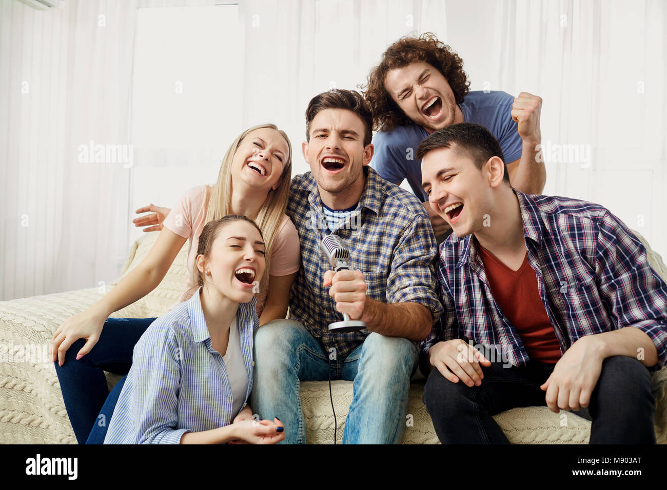 A group of friends with a microphone are singing fun songs indoo Stock Photo