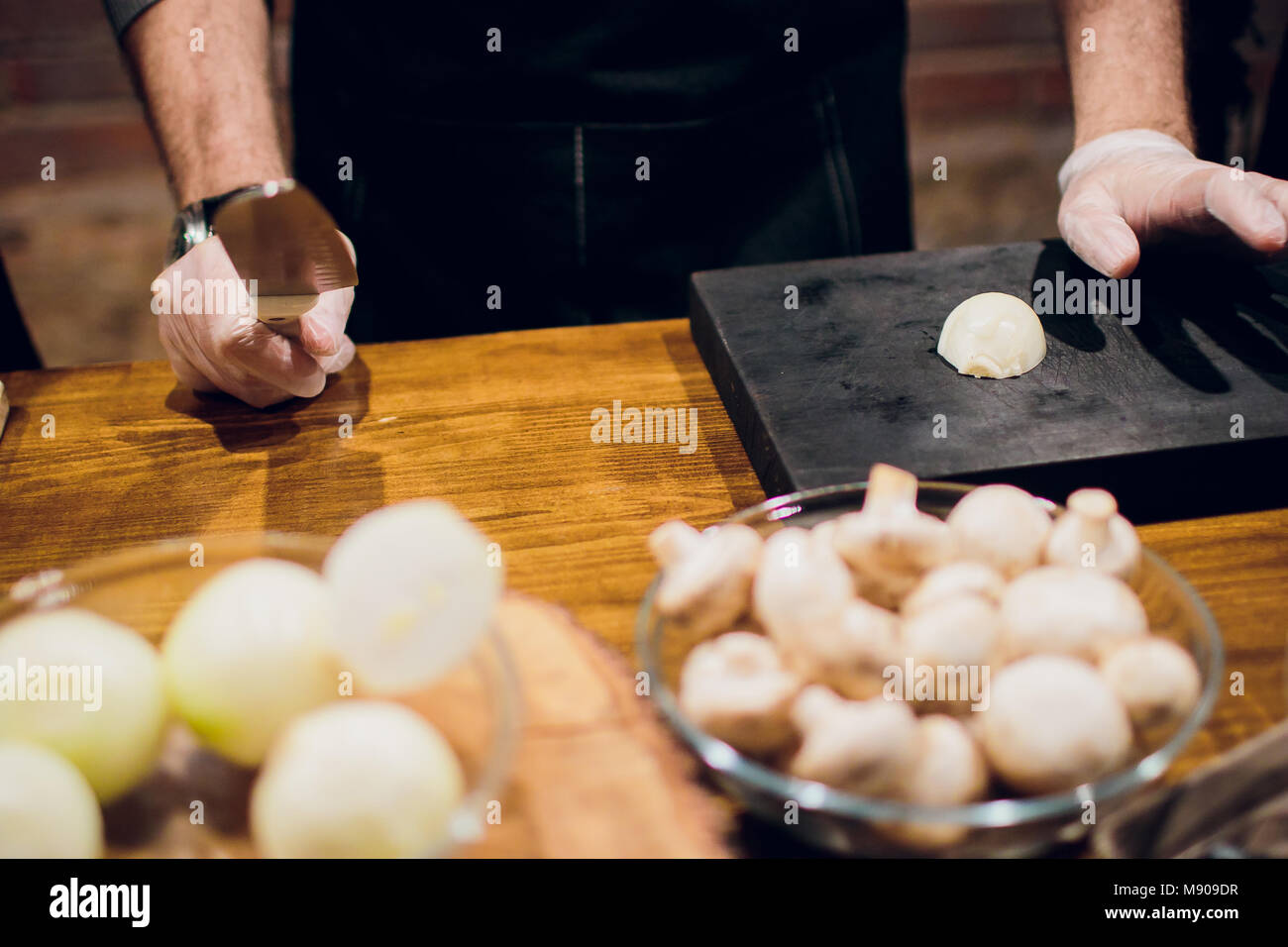 Chef's hands with knife cutting the onion on the wooden board ...