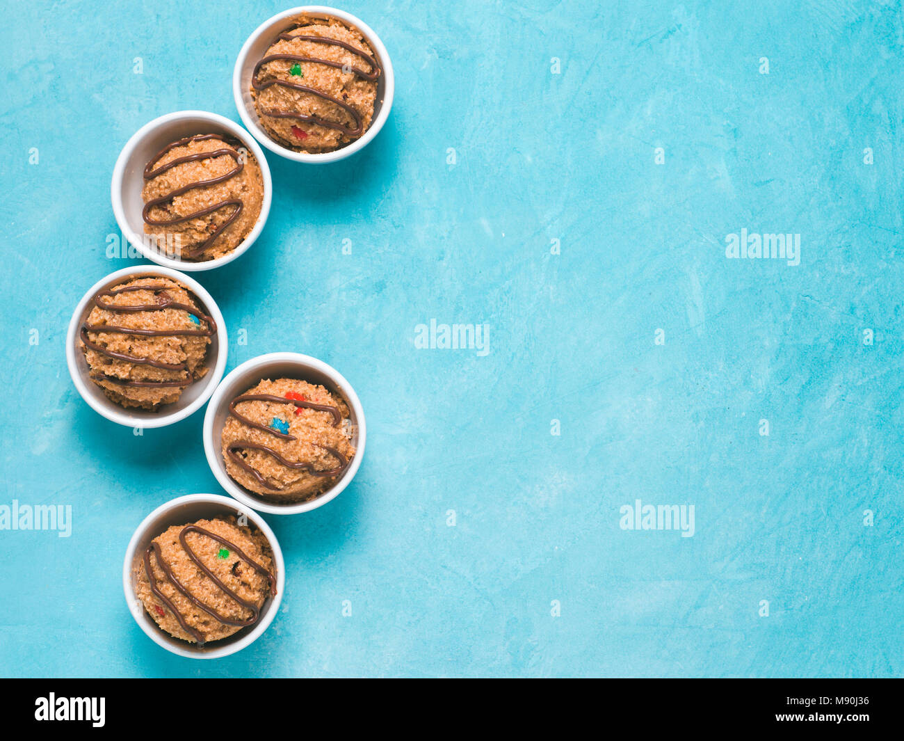 Safe-to-eat raw monster cookie dough in small portion bowl on blue background. Ideas and recipes for kids and toddlers meal. Top view or flat-lay. Copy space for text. Stock Photo