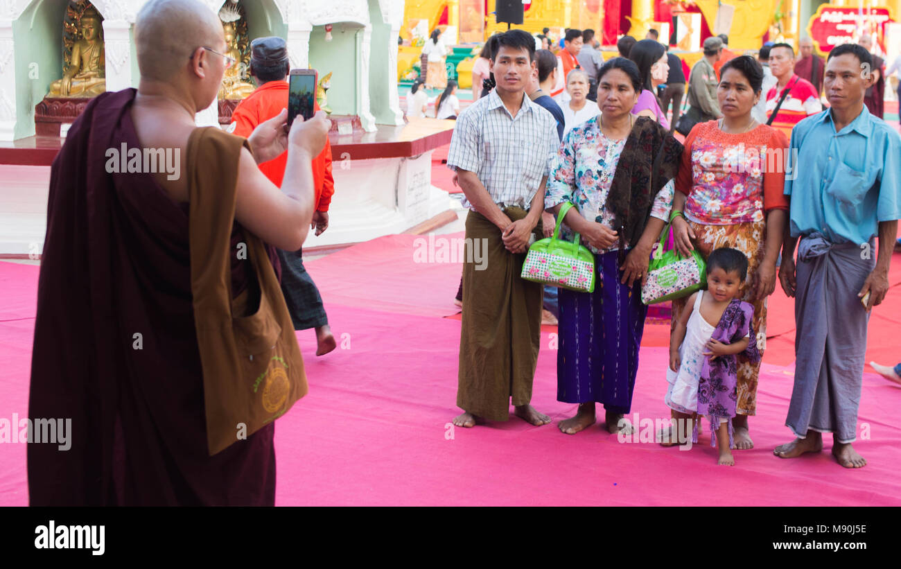 Yangon, Myanmar - February, 15, 2018: a Burmese monk taking picture for a group of Buddhist worshipers at Shwedagong Pagoda Stock Photo