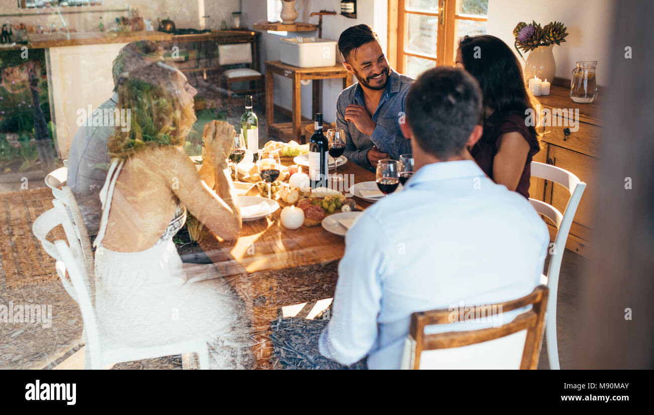 Young friends at a table talking over lunch at home. group of men and women enjoying meal at home together. Stock Photo