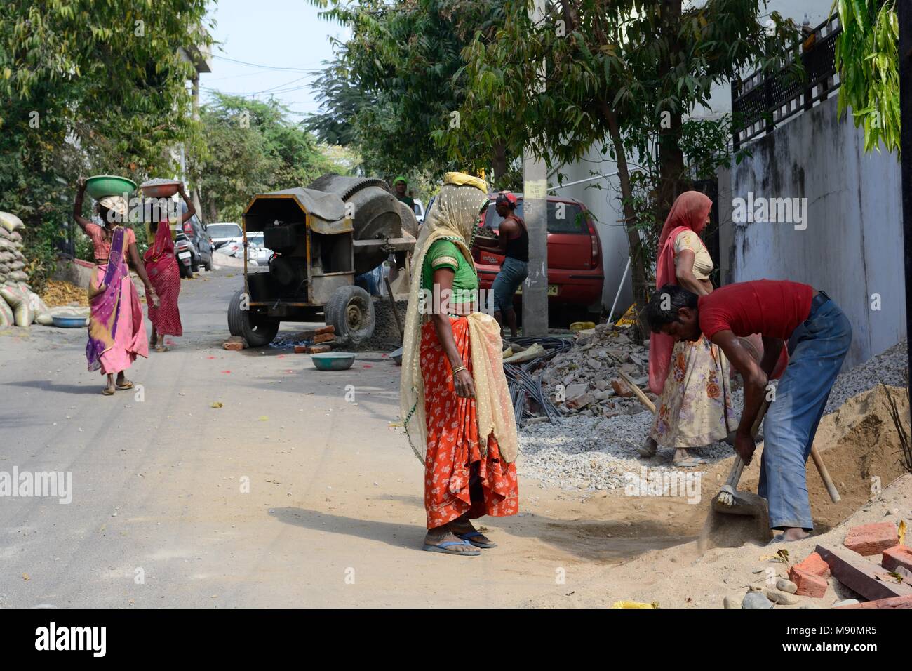 Indian women wearing saris working in construction carrying bowls of sand and stones on their heads to make cement for building Udaipur Rajashan India Stock Photo