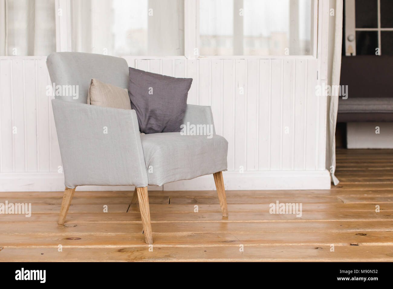 Interior shot of simple comfortable armchair with cushions on wooden floor Stock Photo