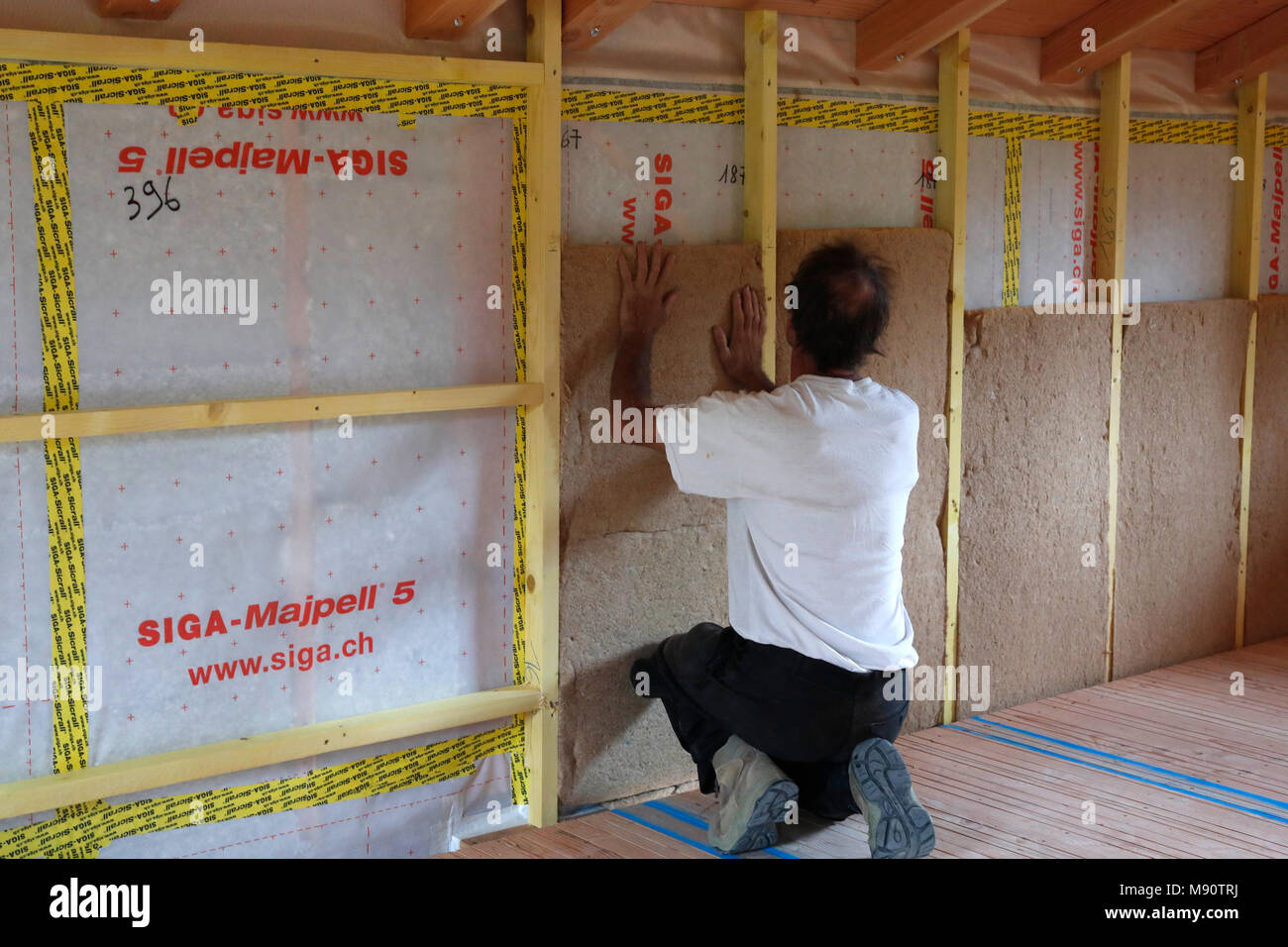 Wooden structure of house under construction. Construction worker installing insulation. Stock Photo