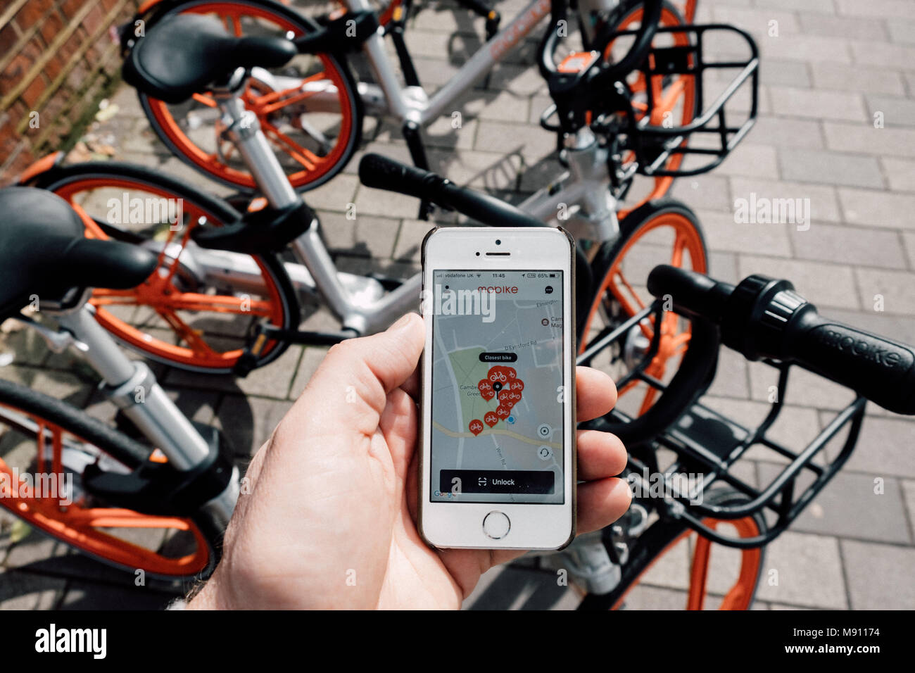 Man holds his iphone with the Mobike app open next to several Mobikes. Mobike is a station-less bicycle-sharing system, smart bike share scheme) dock Stock Photo