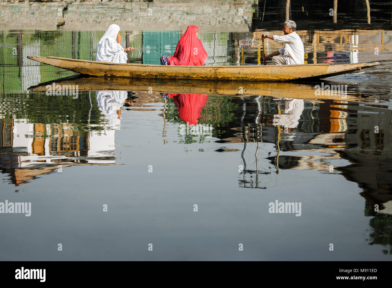 Mirror Image Photo of two Muslim women with back to the camera and boat man ferrying the women across the famous Dal Lake of Srinagar in Kashmir Stock Photo