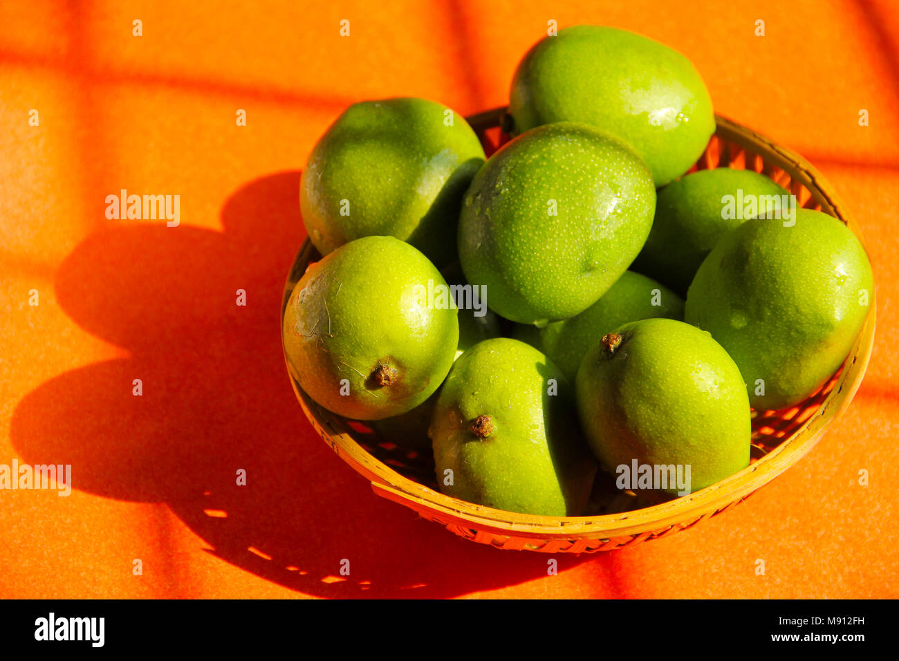 Close up of cane bowl with raw mango fruit in sunlight Stock Photo