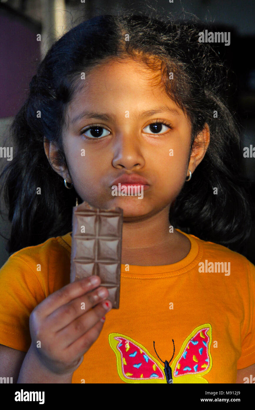 Small girl eating chocalate bar with a serious or guilty expression with sunlight on her face Stock Photo