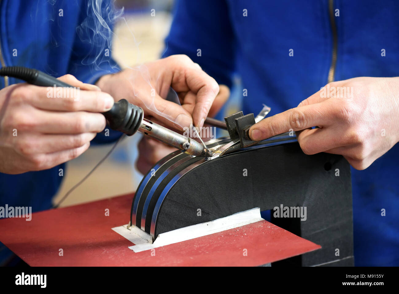 Two blue collar workers soldering electrical transformer in close up Stock Photo