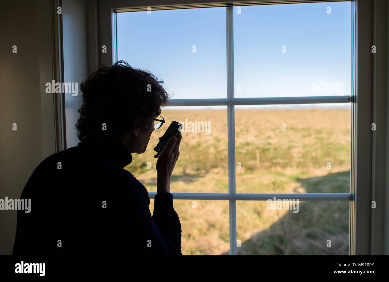 Man using a cell phone near a window. Iceland. Stock Photo