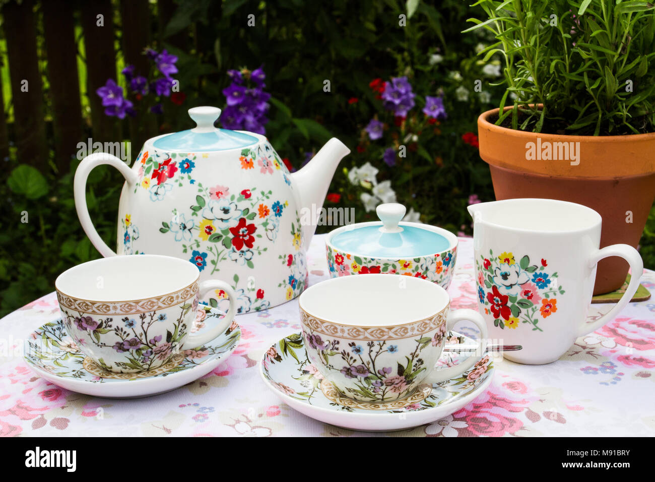 A floral tea service with teapot, cups and saucers and milk jug on a picnic table in an English country garden ready for afternoon tea. Stock Photo