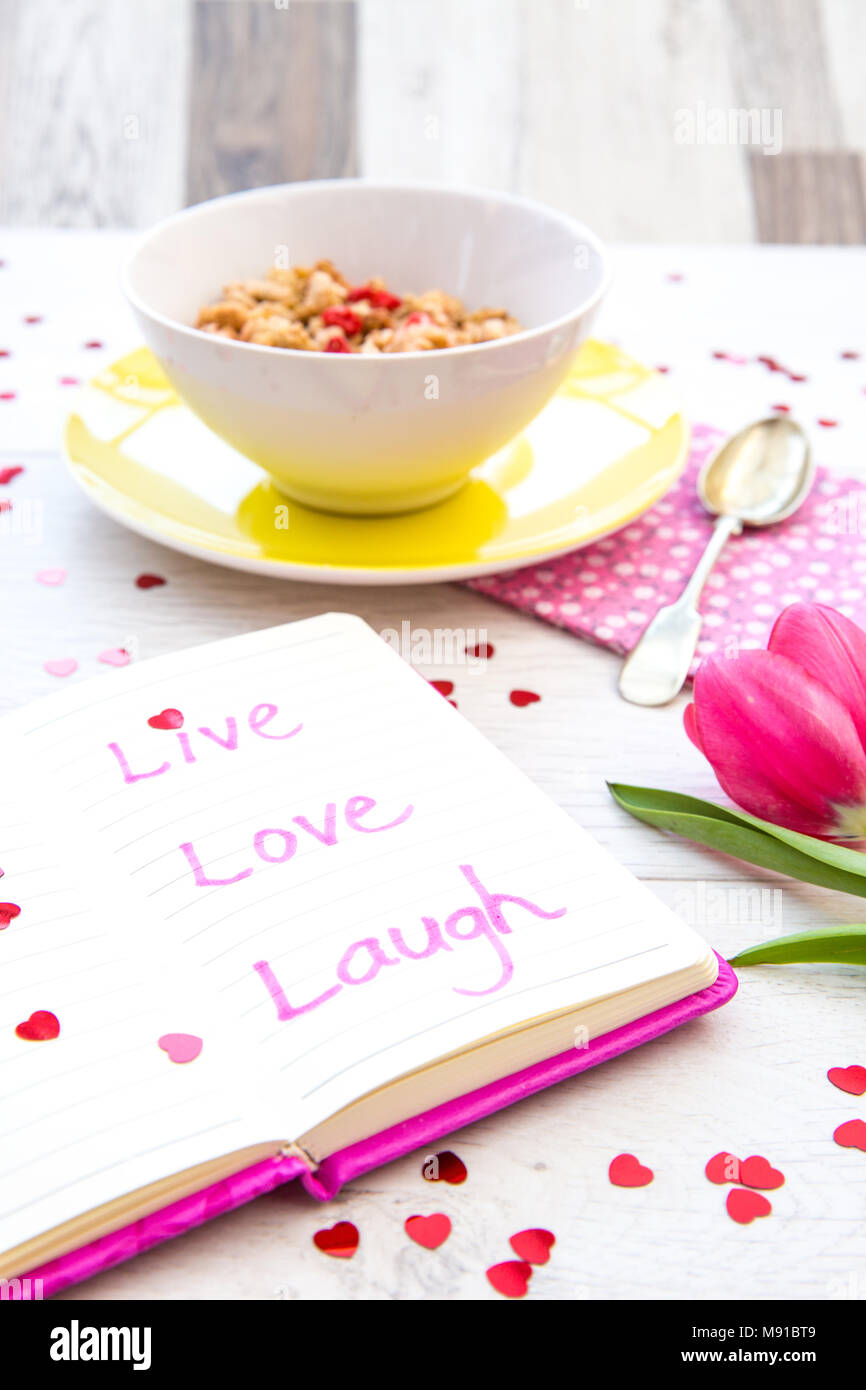 A pink notebook with an inspirational quote saying live, love, laugh in it on a feminine breakfast table top at breakfast. Stock Photo