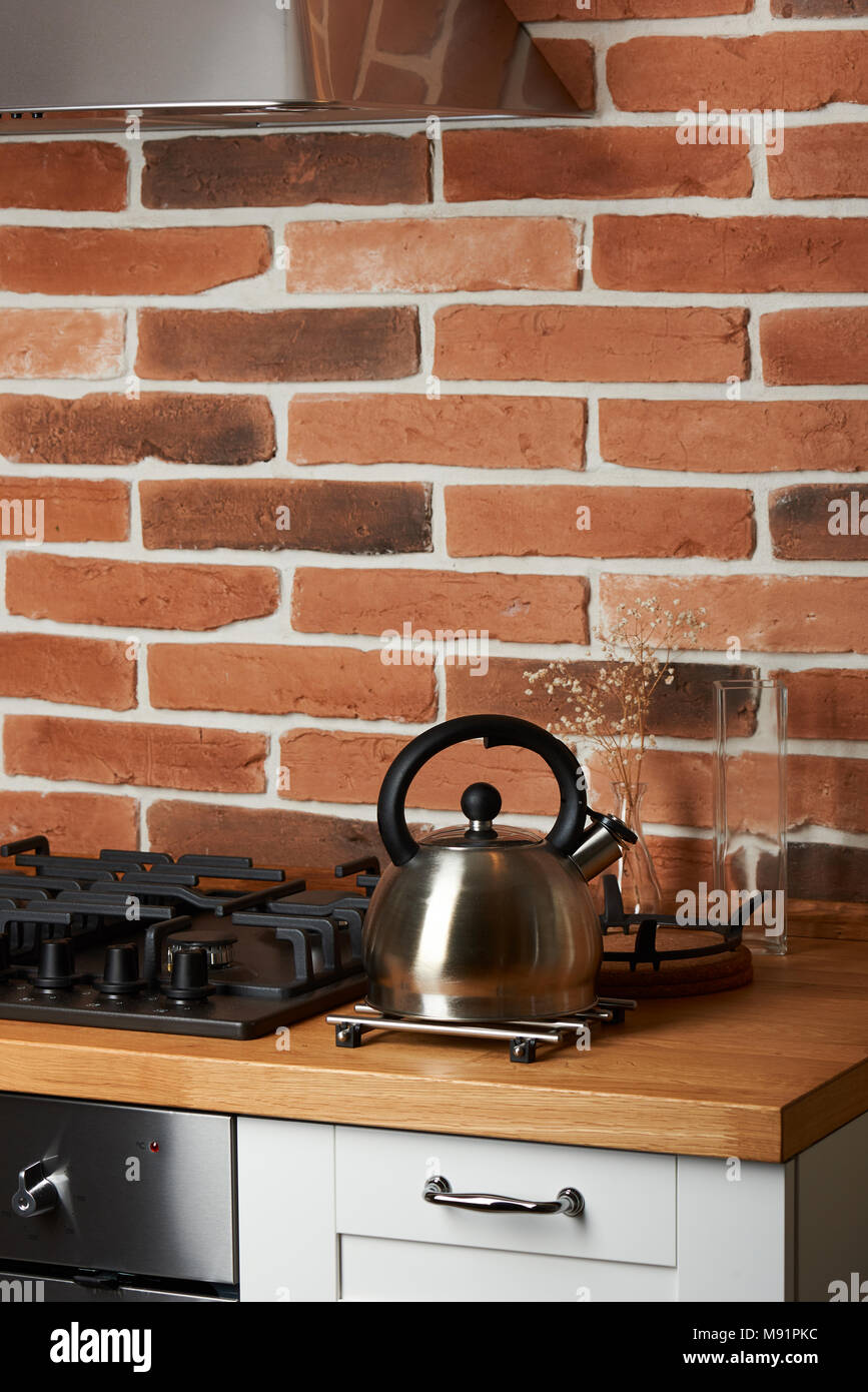 Metal kettle on modern kitchen table with red brick background Stock Photo