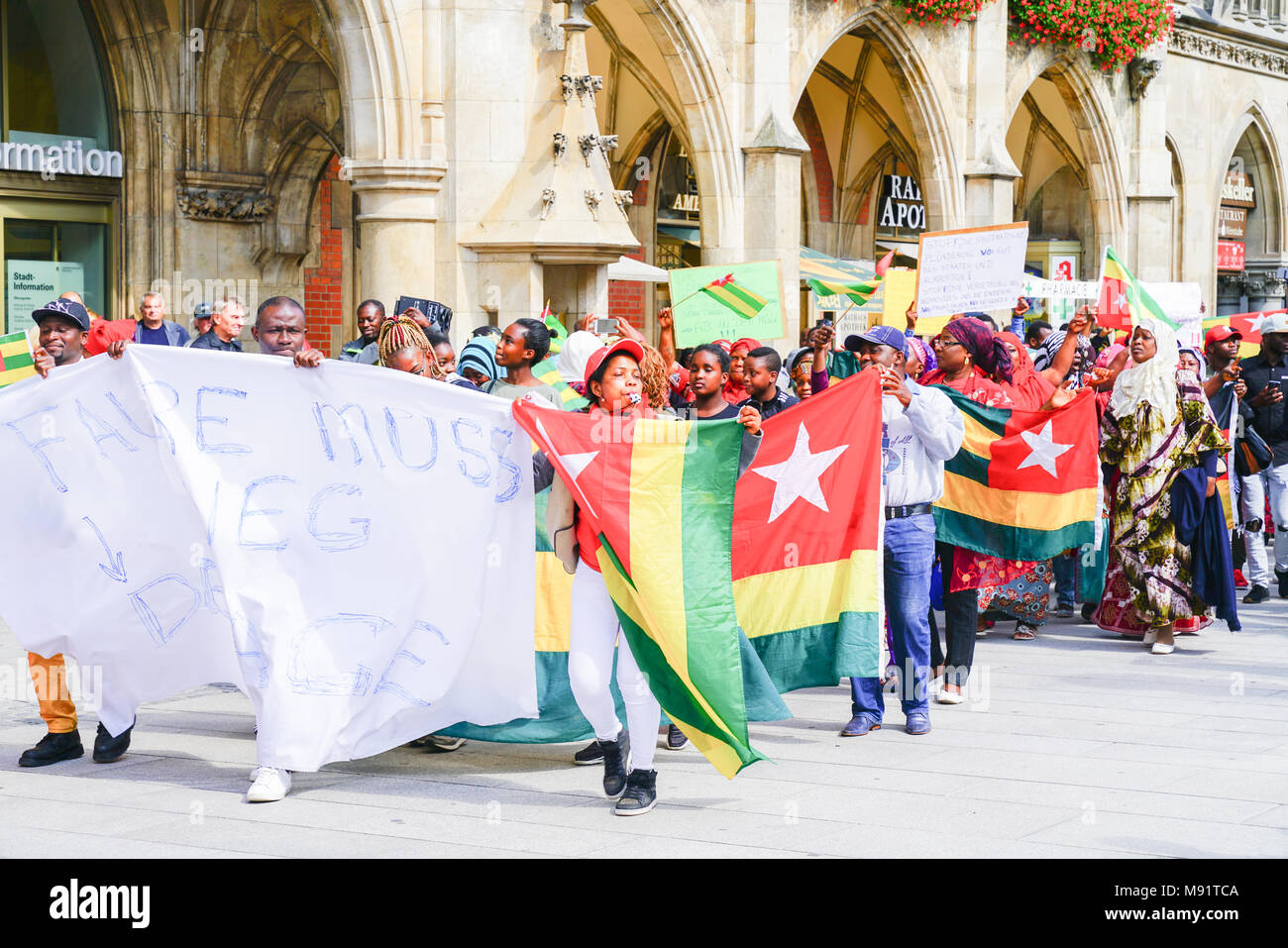MUNICH, GERMANY - SEPTEMBER 8 2017; protestors carrying signs and Togo flags march through tourists in city central square below the gothic city hall. Stock Photo