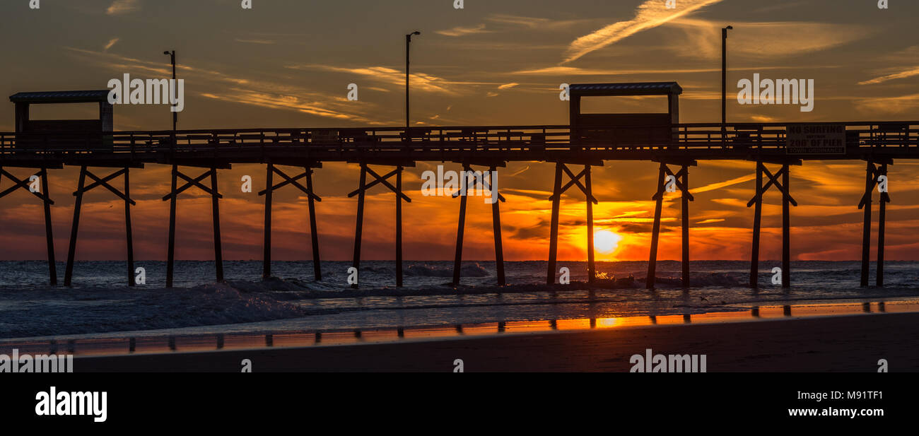 Sunset at the north carolina beach with atlantic beach pier and sunrise with sand, water and reflections in the foreground Stock Photo