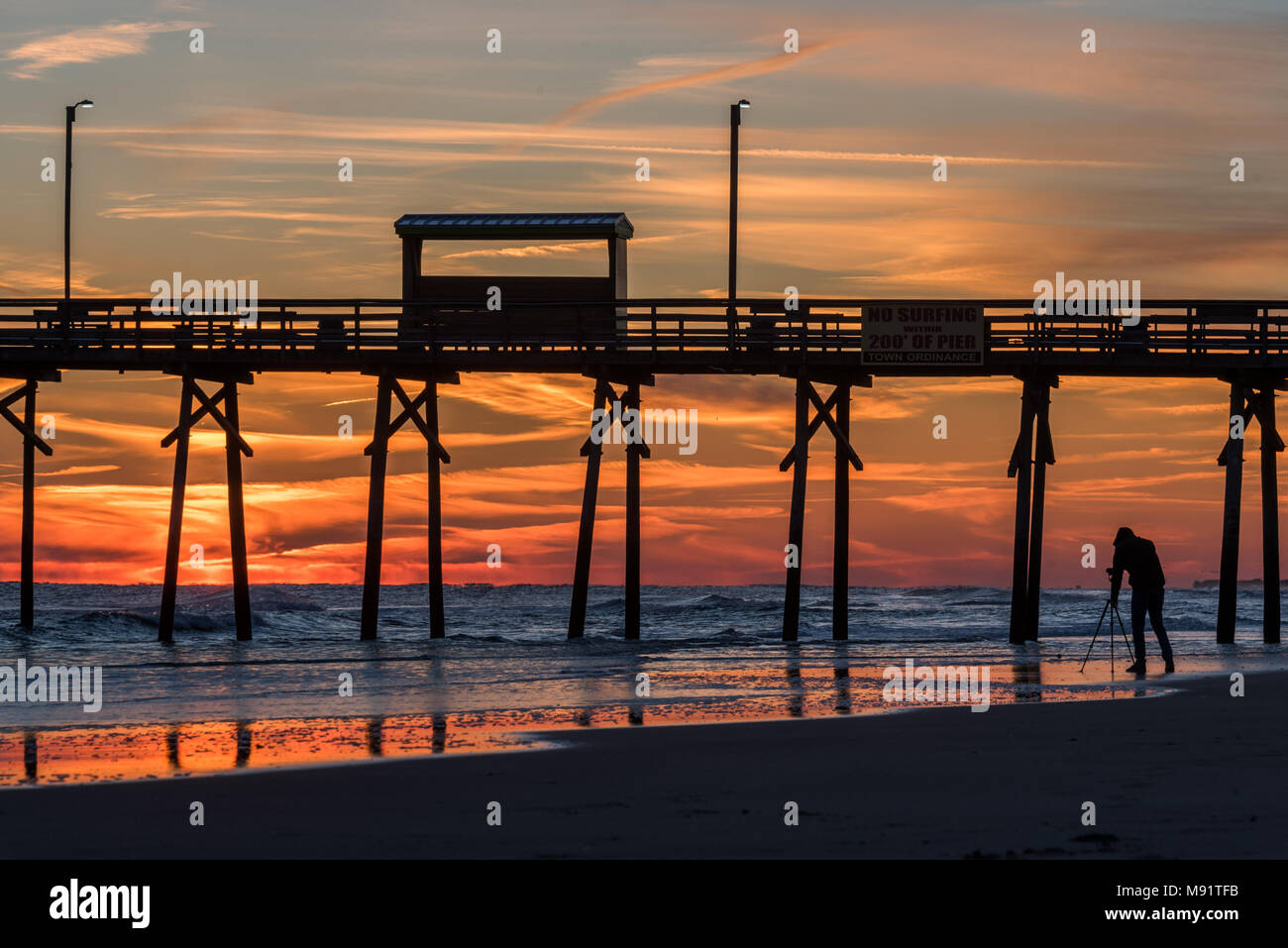 Sunset at the north carolina beach with atlantic beach pier and sunrise with sand, water and reflections in the foreground Stock Photo