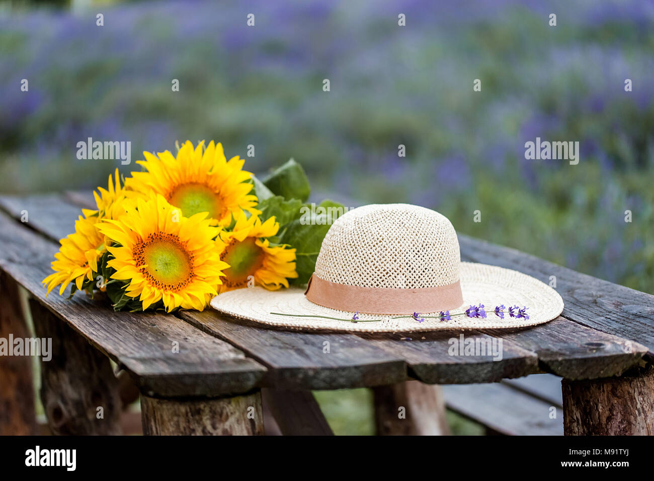 Sunflower bouquet and a straw hat on a wood table at the sunset, over ...