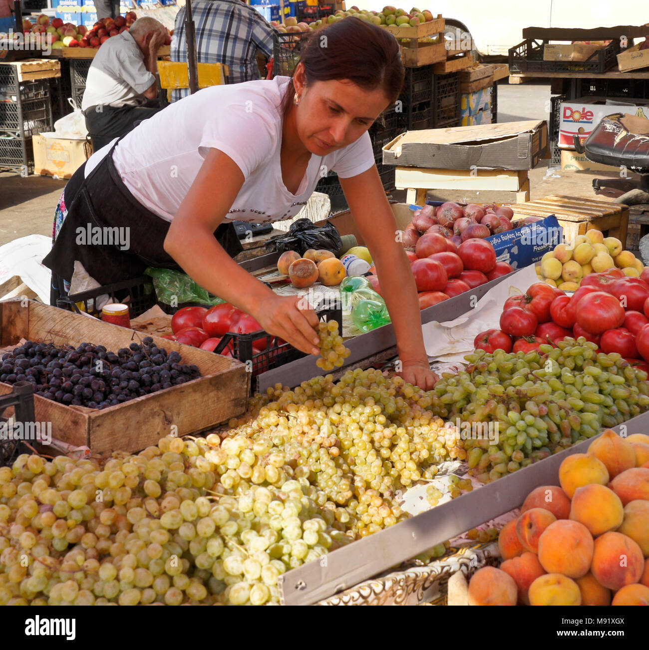 A woman selling fresh produce, including grapes, peaches, and tomatoes, tidies her display at the Dezerters' Bazaar open-air market, Tbilisi, Georgia Stock Photo