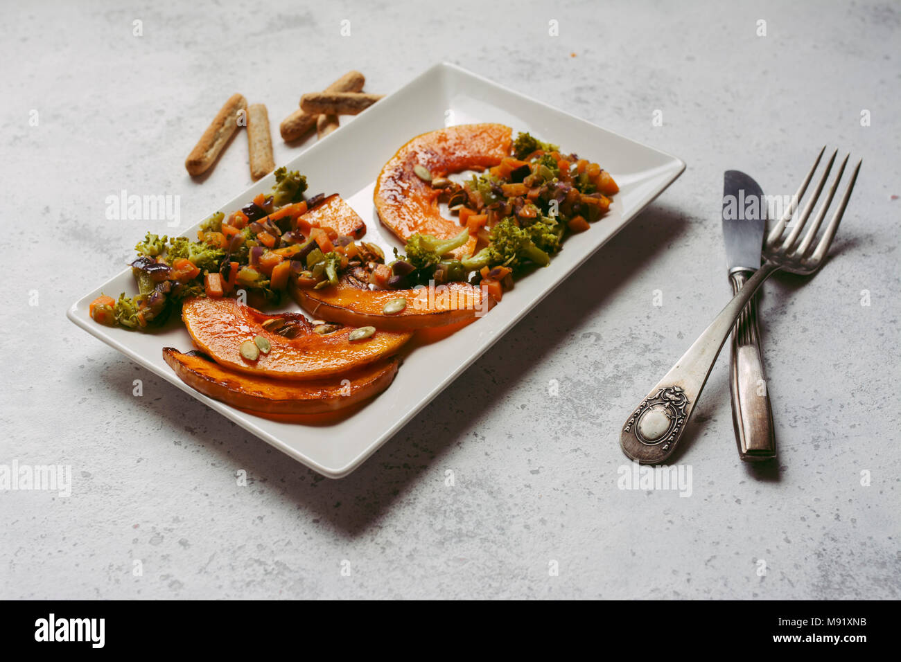 sliced baked pumpkin, with broccoli and assorted vegetables, on rectangular white plate Stock Photo