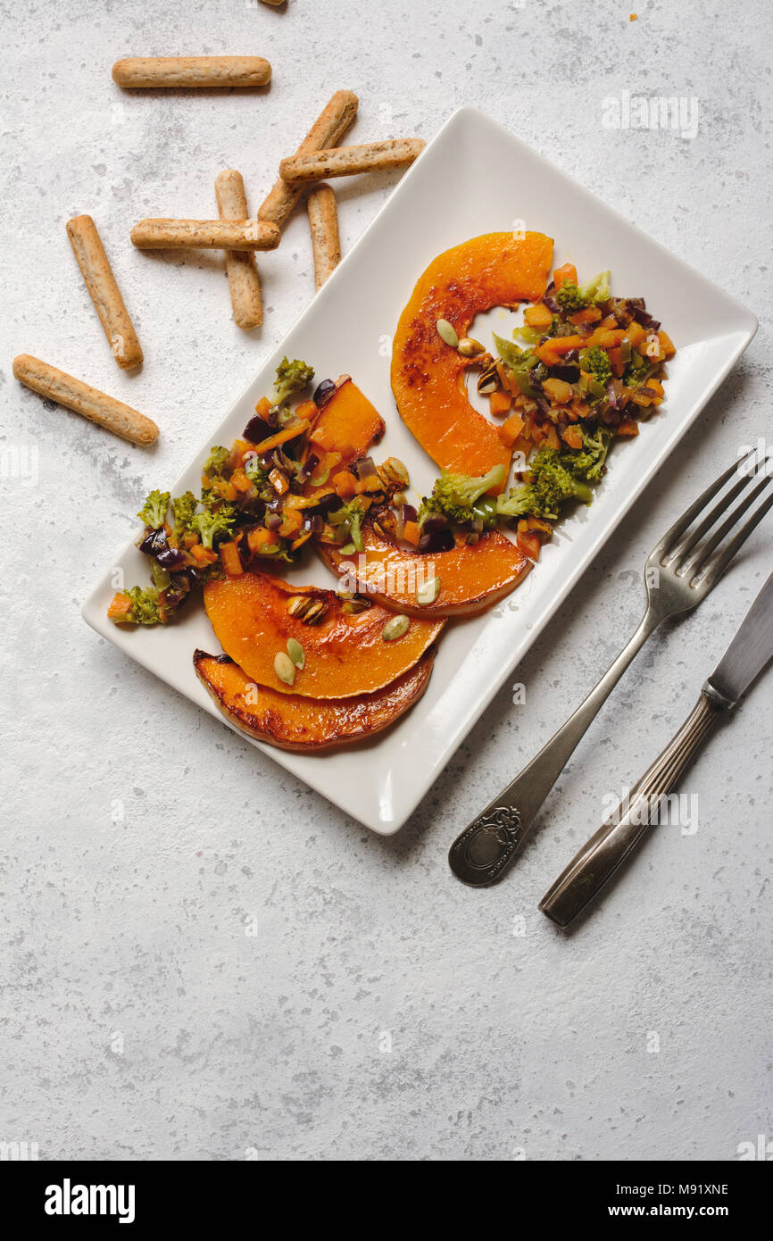 sliced baked pumpkin, with broccoli and assorted vegetables, on rectangular white plate, from above Stock Photo
