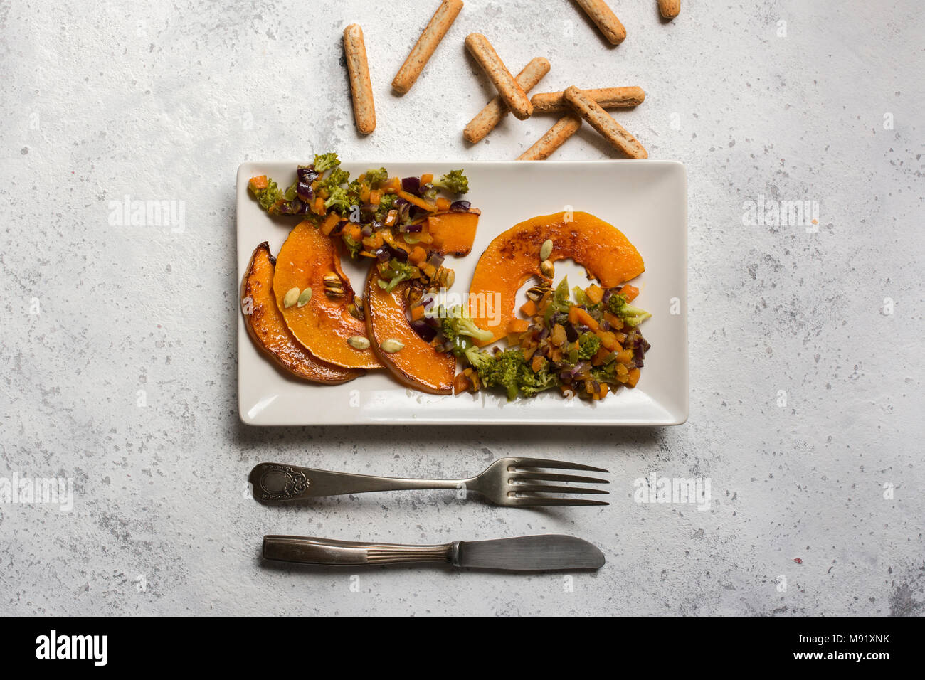 sliced baked pumpkin, with broccoli and assorted vegetables, on rectangular white plate, from above Stock Photo