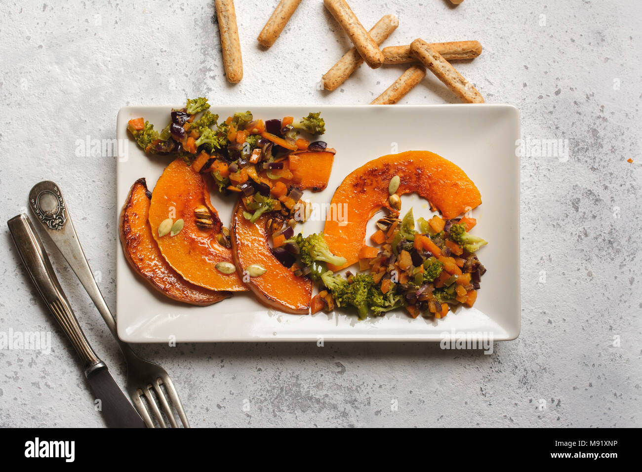 sliced baked pumpkin, with broccoli and assorted vegetables, on rectangular white plate Stock Photo