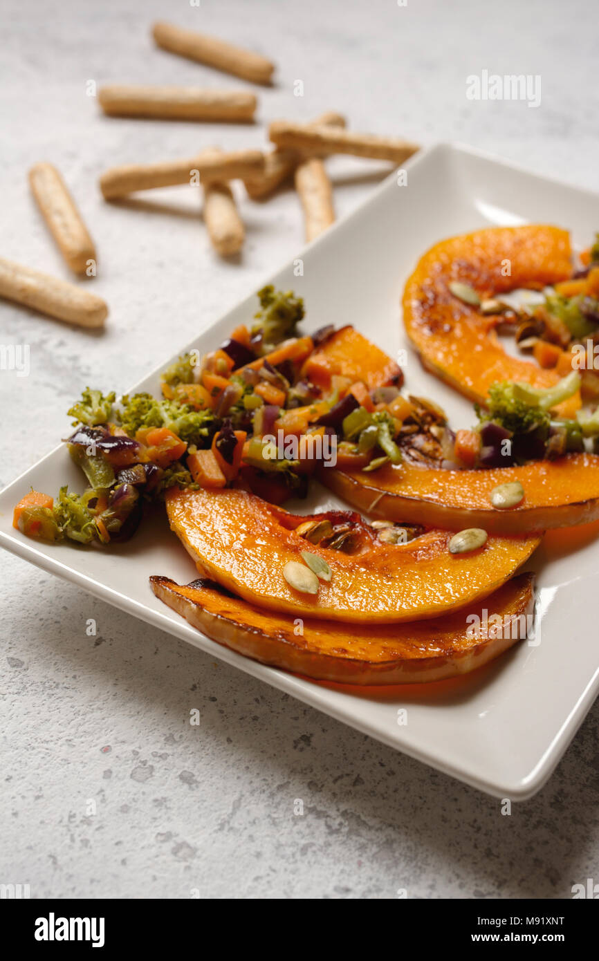 sliced baked pumpkin, with broccoli and assorted vegetables, on rectangular white plate Stock Photo