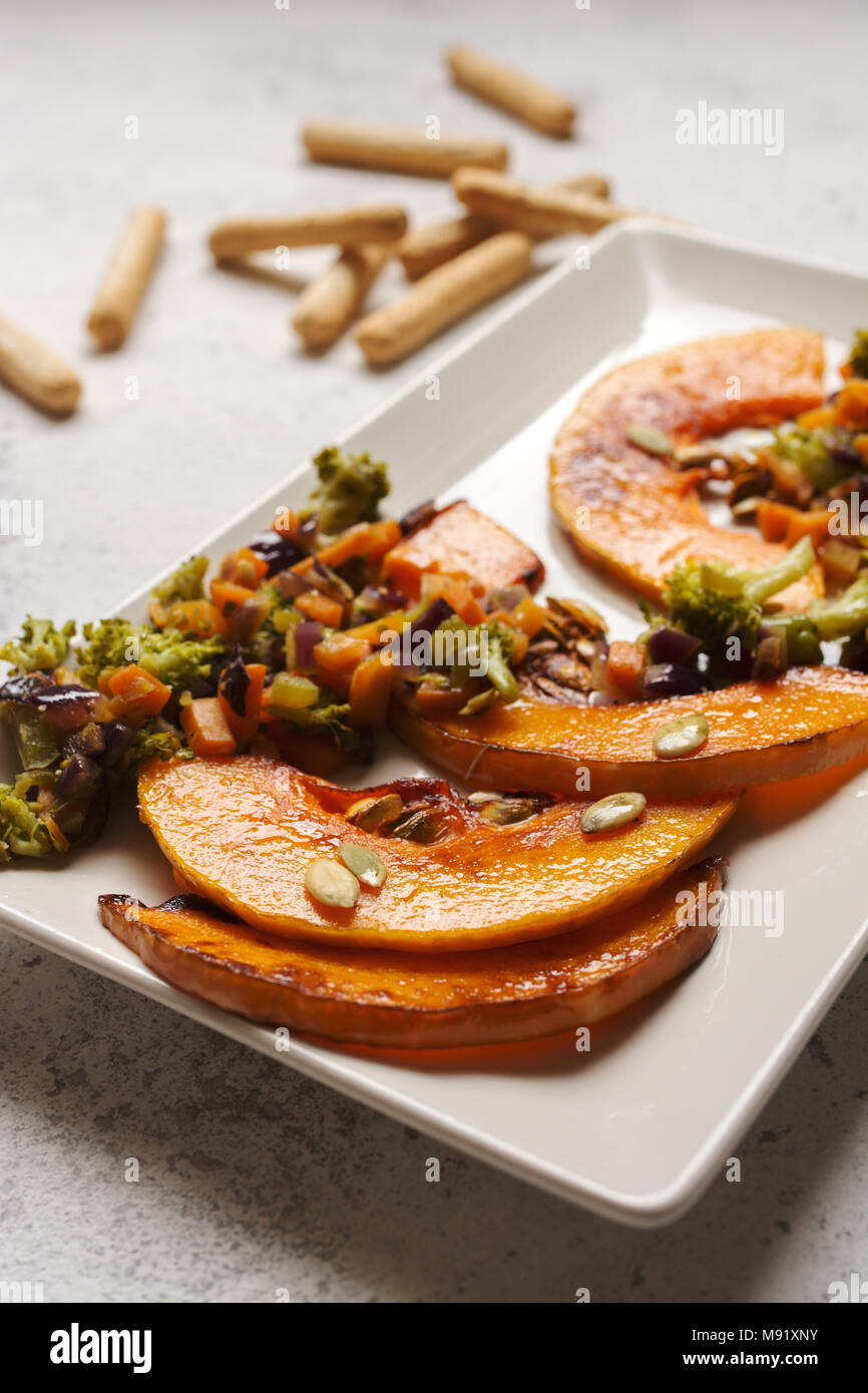 sliced baked pumpkin, with broccoli and assorted vegetables, on rectangular white plate Stock Photo