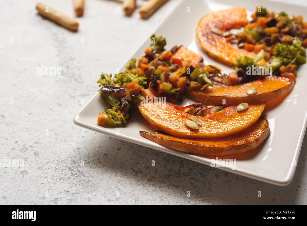 sliced baked pumpkin, with broccoli and assorted vegetables, on rectangular white plate Stock Photo