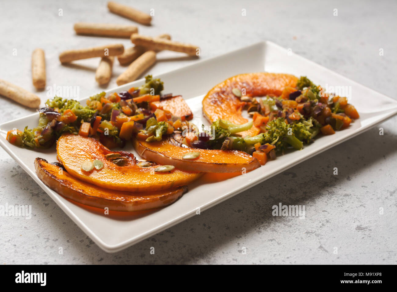 sliced baked pumpkin, with broccoli and assorted vegetables, on rectangular white plate Stock Photo
