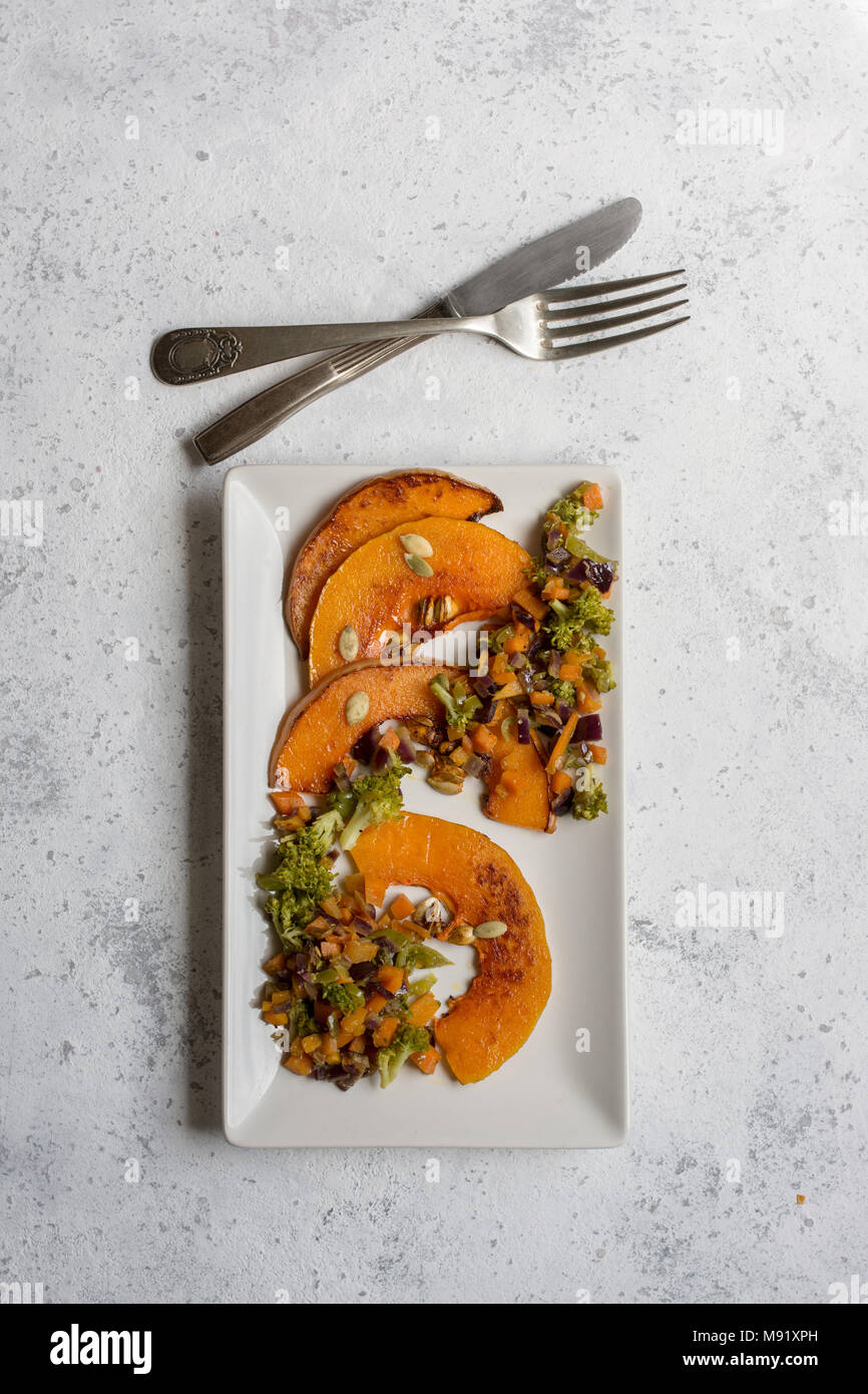sliced baked pumpkin, with broccoli and assorted vegetables, on rectangular white plate, from above Stock Photo