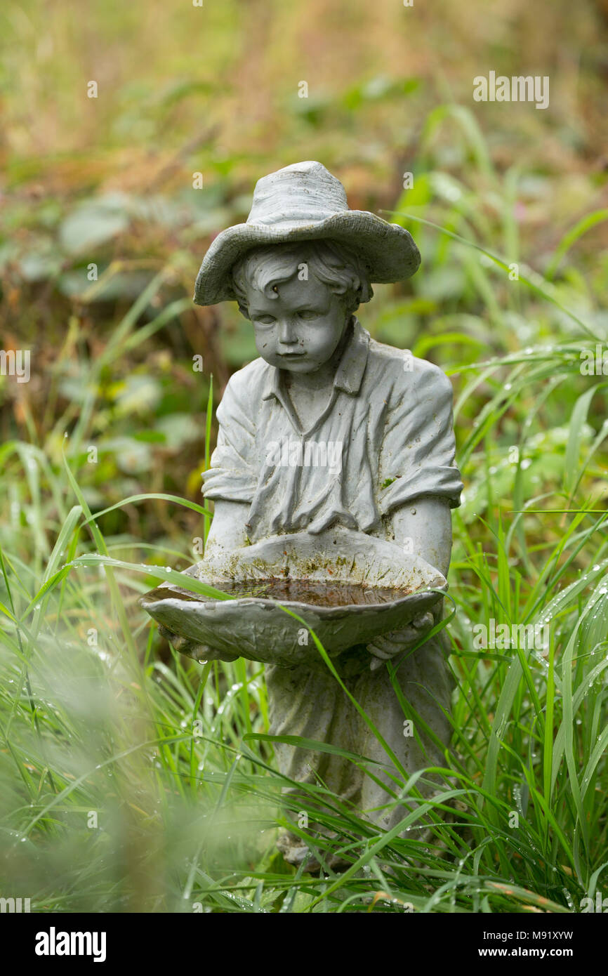 Stone statue of a young boy holding a bird bath in a country garden, Lancashire UK. September 2018 Stock Photo