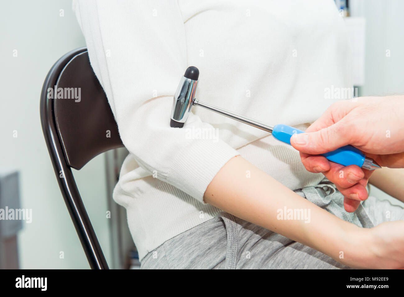 Neurological physical examination of the elbow flexion reflex. Doctor neurologist with a neurological hammer in his hand checks the status of the patient's reflexes in office in hospital. Stock Photo