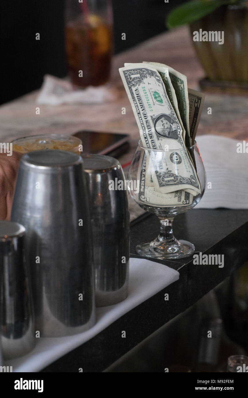 Cash tips in a cocktail glass on bar counter top. Customers give money