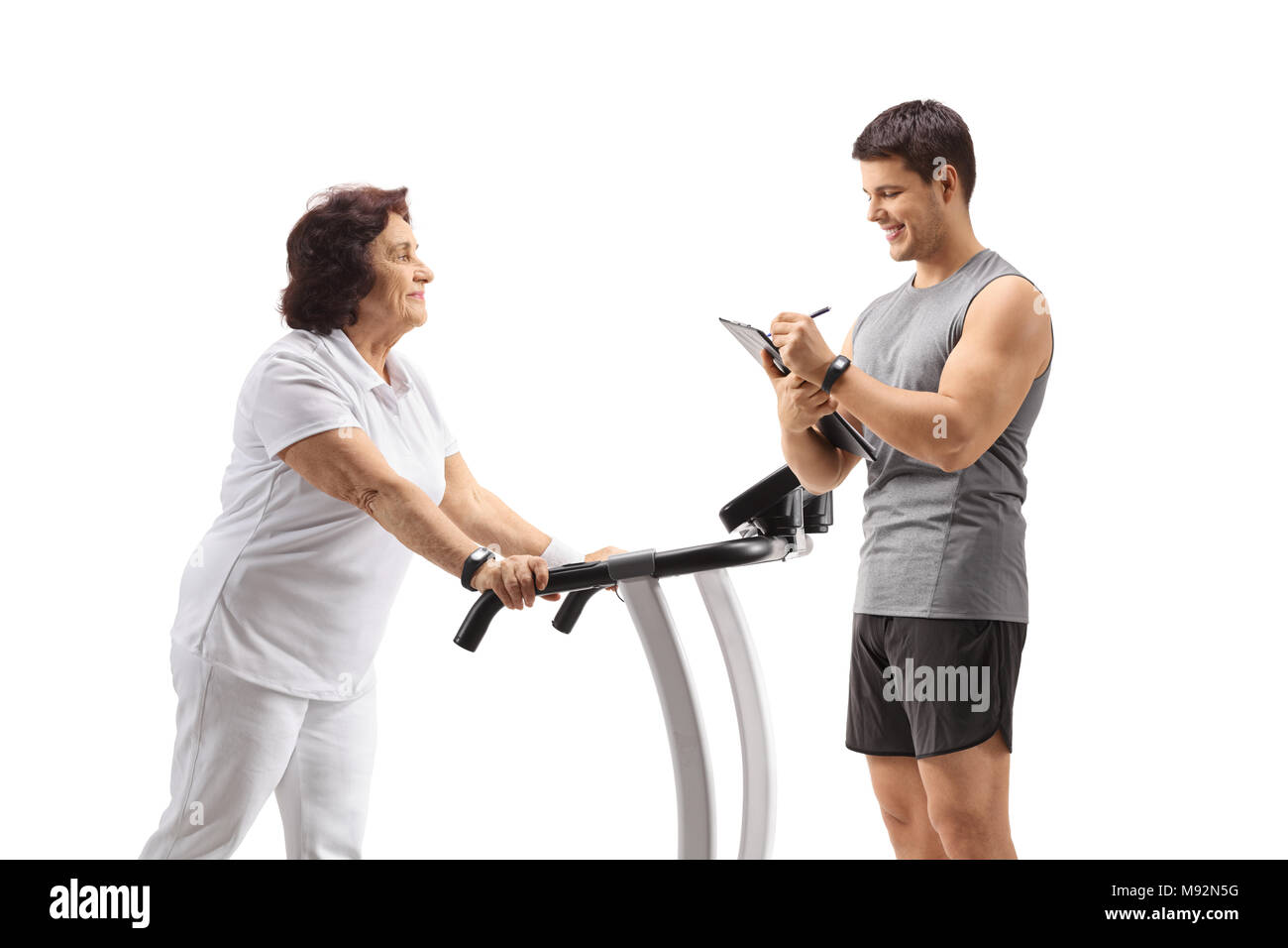 Mature woman exercising on a treadmill with a personal trainer writing in a clipboard isolated on white background Stock Photo