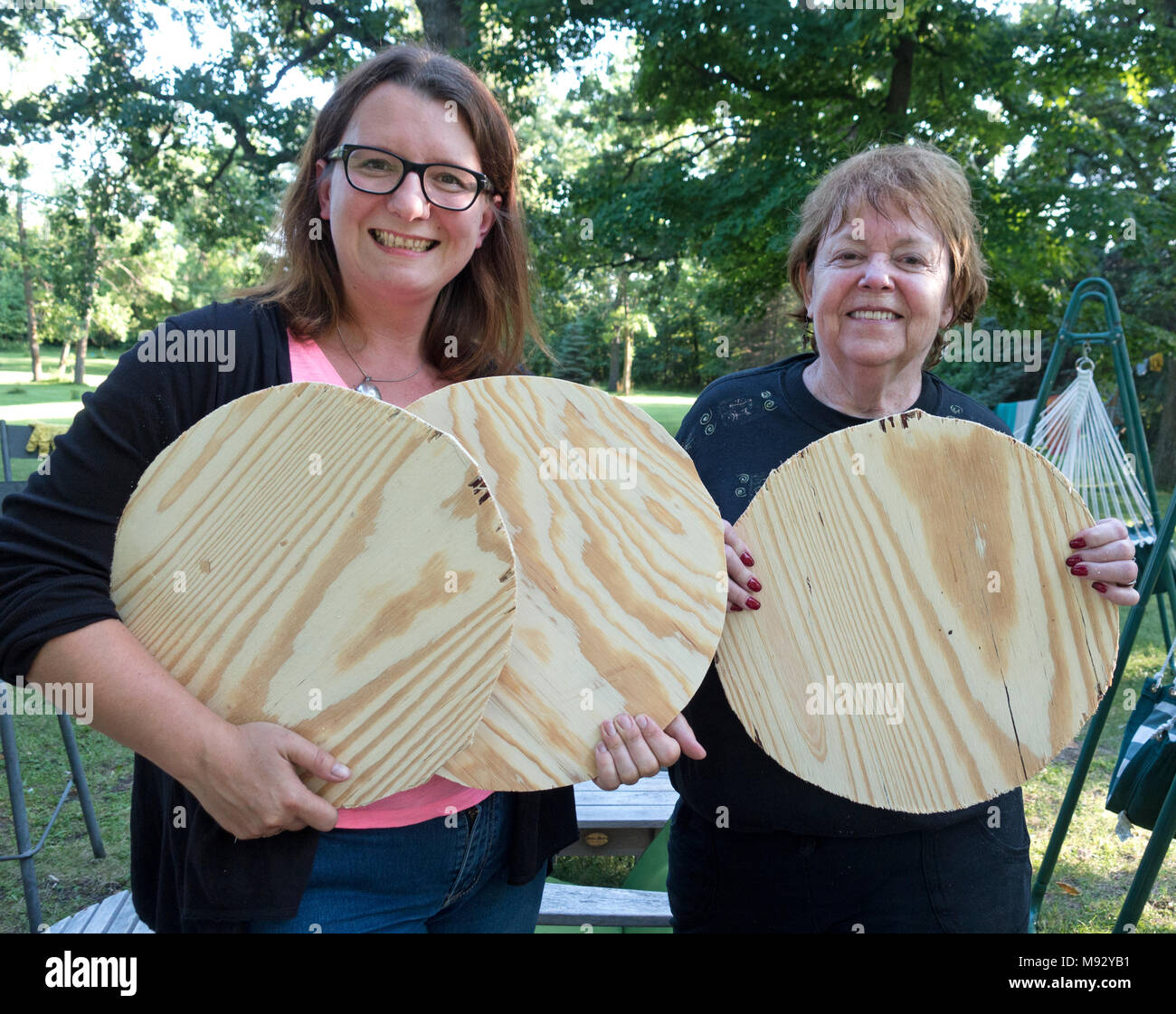 Two proud women holding up circle cut-outs they just made from a sheet of plywood for remodeling barstool seats. Clitherall Minnesota MN USA Stock Photo