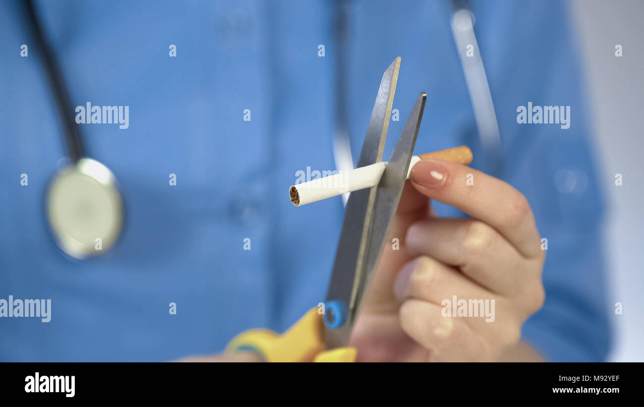 Doctors hands cutting cigarette with scissors, anti-tobacco campaign, bad habit Stock Photo